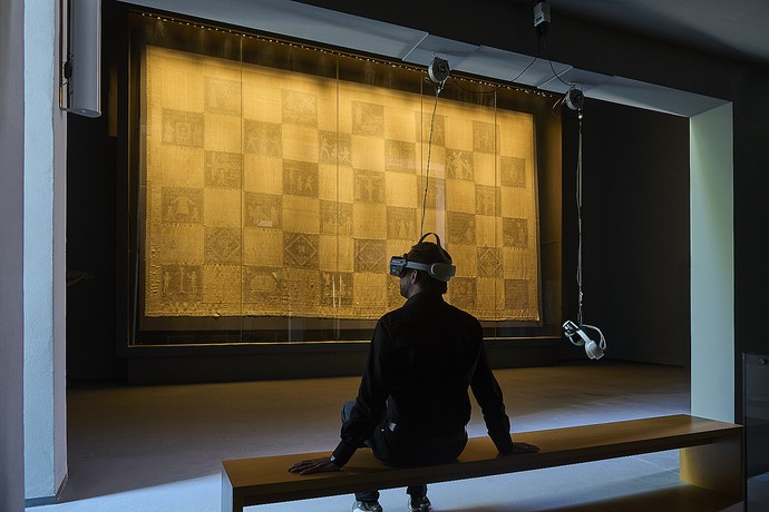 Ansicht des Ausstellungsbereichs mit dem Telgter Hungertuch im Hintergrund und einem Benutzer mit VR-Brille in der Mitte des Bildes